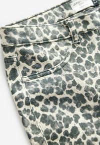 Cropped jersey pants with a green and cream leopard print. Features a waistband, front pocket, and stitched seams for added texture.