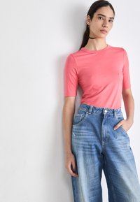 Top cor-de-rosa de manga curta, ajustado, combinado com jeans de perna larga de cintura alta em azul claro, com detalhes desgastados e bolsos frontais.