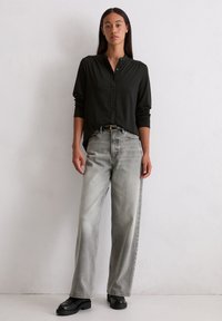 Chemise noire à manches longues avec boutons, jean gris à jambe large avec une finition délavée et bottes à plateforme noires. Design simple, sans motifs visibles.