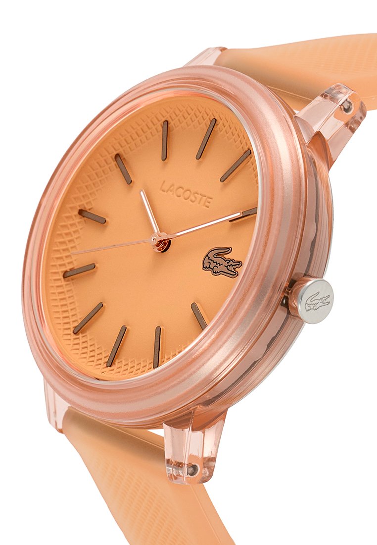 Reloj Lacoste con caja transparente en color durazno, correa de silicona a juego, dial texturizado, manecillas plateadas y detalle del logo cerca de la corona.