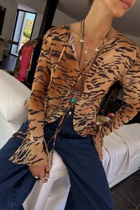 Brown and black tiger-striped sheer blouse with long sleeves and flared cuffs, layered over a tank top, paired with dark denim jeans.