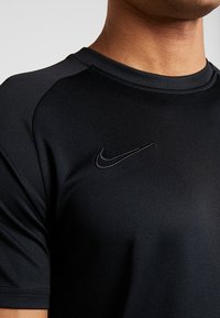 Svart Nike träningströja med rund halsringning, korta ärmar och en liten broderad logotyp på övre vänstra bröstet. Slät, elastisk tyg.
