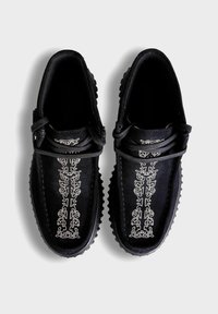 Schwarze Wildlederschuhe mit strukturierten Gummisohlen, ausgestattet mit aufwendiger weißer Stickerei entlang der Mitte und Schnürdesign.