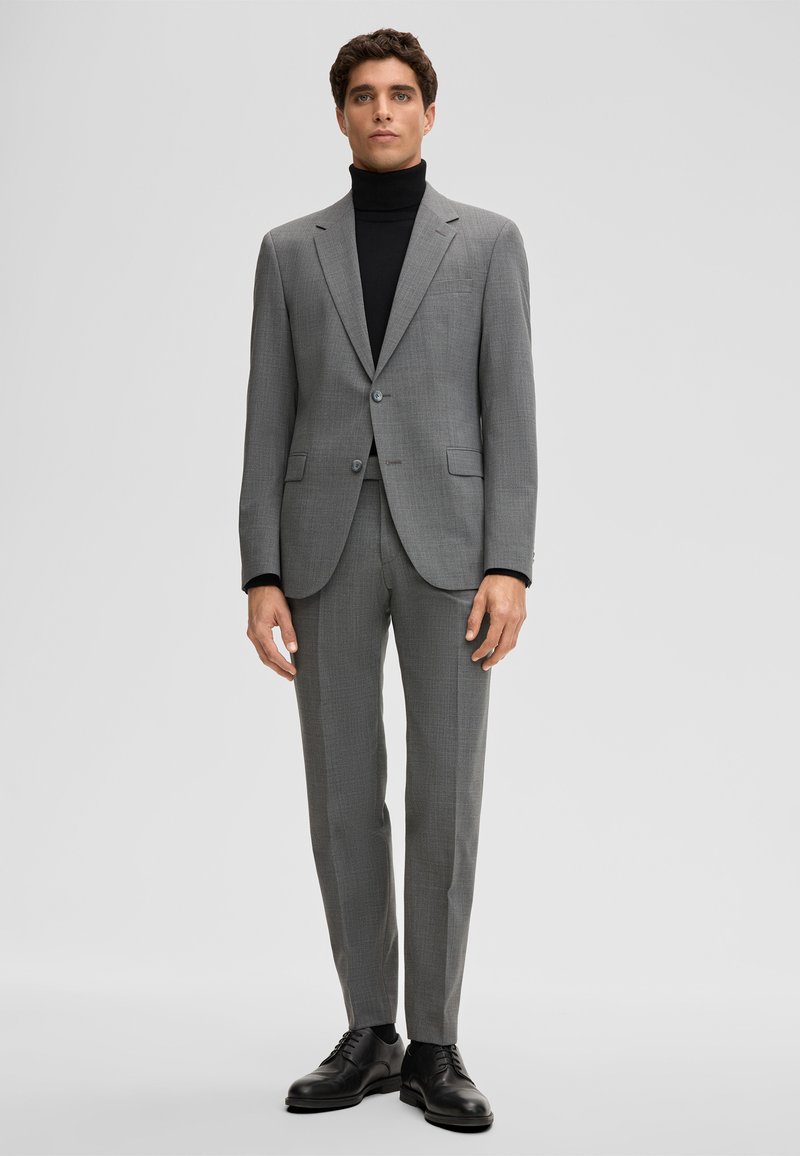 Abito grigio in tessuto strutturato, composto da blazer monopetto, pantaloni slim-fit e dolcevita nero. Scarpe in pelle nera incluse.