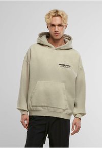 Felpa con cappuccio in beige chiaro, realizzata in cotone, dotata di una tasca frontale e di testo ricamato in nero sul lato sinistro del petto.