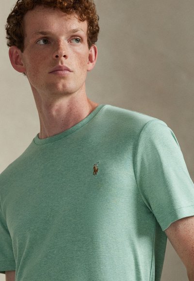 Světle zelené tričko s krátkými rukávy z měkké látky, s malým vyšívaným logem na levé straně hrudi a kulatým výstřihem.