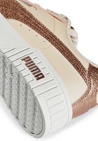 Gros plan d'une basket Puma blanche et or rose montrant une semelle texturée et une bande latérale métallique.