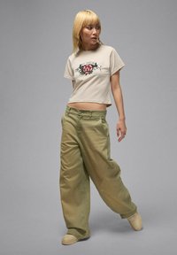 Beige Cropped-T-Shirt mit Rosenmotiv, kombiniert mit locker sitzender olivgrüner Hose. Weicher Stoff, leichter Glanz und eine entspannte Silhouette.