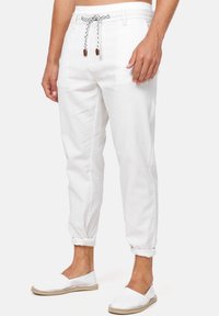 Weiße Leinenhose mit elastischem Bund, schwarz-weißer Kordel und umgeschlagenen Säumen. Kombiniert mit weißen Espadrilles.