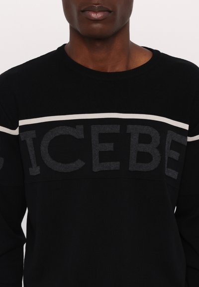 Pull noir avec une finition texturée, arborant un logo "ICEBE" gris audacieux sur la poitrine et des rayures horizontales blanches. Conception à col rond.