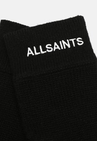 Svarta stickade strumpor med ribbat mudd och vit "ALLSAINTS" brodyr, som visar en mjuk textur och en enkel design.