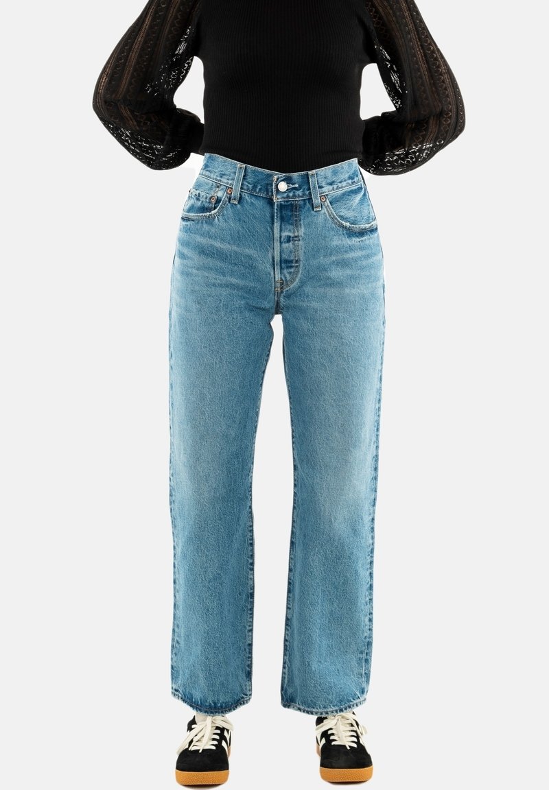Lichtblauwe hoge taille jeans met een rechte pijpdesign, voorzien van vijf zakken en een knoopsluiting. De schoenen zijn zwart met een tan zool.