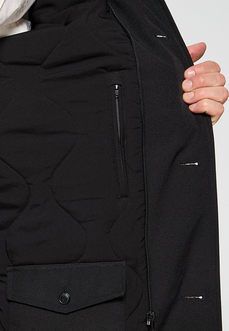 Zwarte geïsoleerde jasinterieur met een gequilt patroon, voorzien van een ritszak en een flapzak met knoopsluiting.