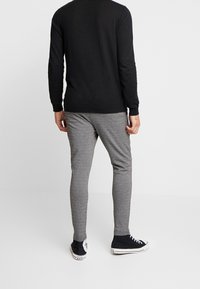 Czarna koszula z długim rękawem, wykonana z lekkiego materiału, zestawiona z szarymi, teksturowanymi spodniami slim-fit oraz czarnymi butami typu high-top.