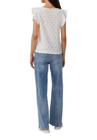 Weiße Bluse mit Lochmuster, Rüschensäumen, kombiniert mit hellblauen weit geschnittenen Jeans und hellen Schuhen.
