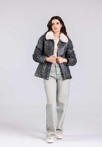 Giacca di pelle grigia con collare in pelliccia sintetica bianca, dotata di chiusura con zip, tasche laterali e vestibilità ampia. Abbinata a jeans in denim chiaro.