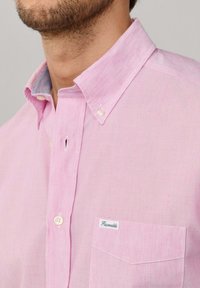 Man in lichtroze overhemd met knoopsluiting, knoopkraag en een klein zakje met het label "Façonnable."