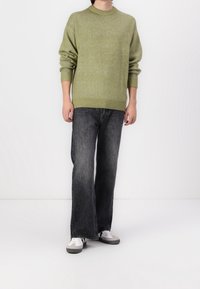 Zielony sweter na drutach z okrągłym dekoltem i ściągaczem u dołu, zestawiony z czarnymi szerokimi jeansami z przetarciami oraz białymi trampkami z szarymi akcentami.