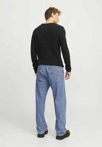 Black ribbed sweater paired with light blue relaxed-fit denim jeans. The sweater features a crew neck and fitted cuffs; jeans display back pockets.