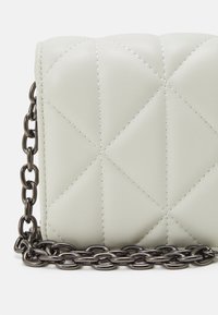 Lekka zielona torebka z pikowanego sztucznego skóry z ciemnym metalowym paskiem łańcuchowym i kontrastującym białym przeszyciem wzdłuż diamentowych wzorów.