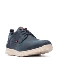 Zapatillas de cuero azul con una superficie texturizada, que cuentan con una suela de goma beige, diseño de cordones y sutiles acentos en rojo y blanco.