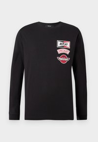 Black long-sleeve shirt with three red and white patches on the left chest reading "REPLAY," "SPECIALIST," and a winged emblem.
