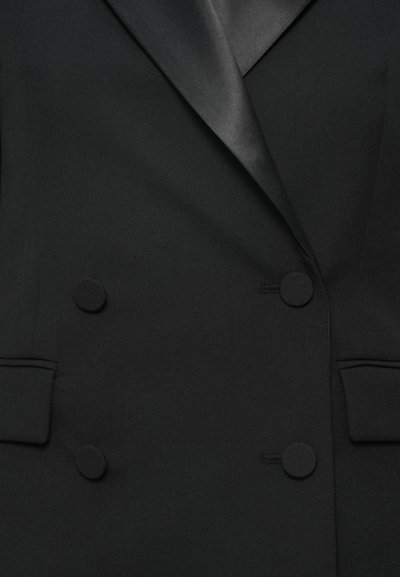 Blazer noir à double boutonnage en tissu texturé. Il présente des revers en notch, deux poches avant et de grands boutons assortis.