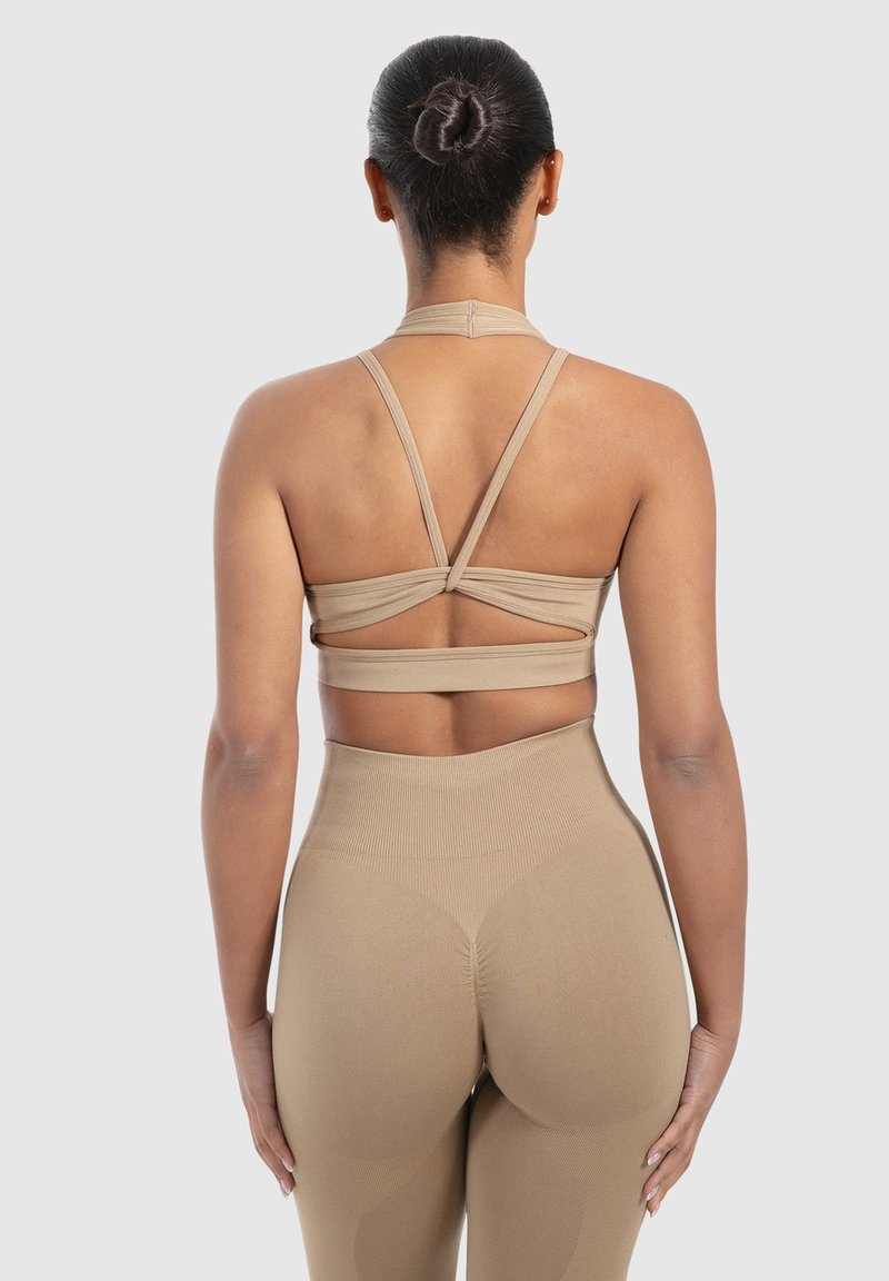 Top de sport beige avec des bretelles croisées et un dos ouvert, associé à un legging taille haute avec un tissu texturé et un design sans coutures.
