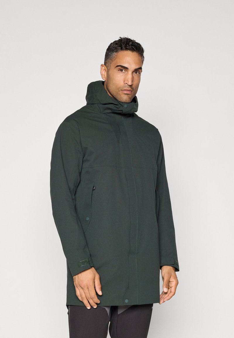 Mørkegrøn vandtæt jakke med høj krave, justerbar hætte, sidelommer og velcro-ærmeafslutninger. Glat tekstur, minimalistisk design.