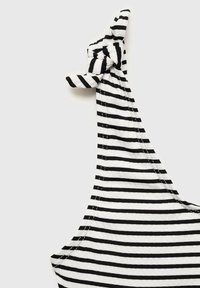Črno-bela striped bluza s vozlom na rami. Narejena iz mehke, raztegljive tkanine, z vidnimi šivi ob robovih.