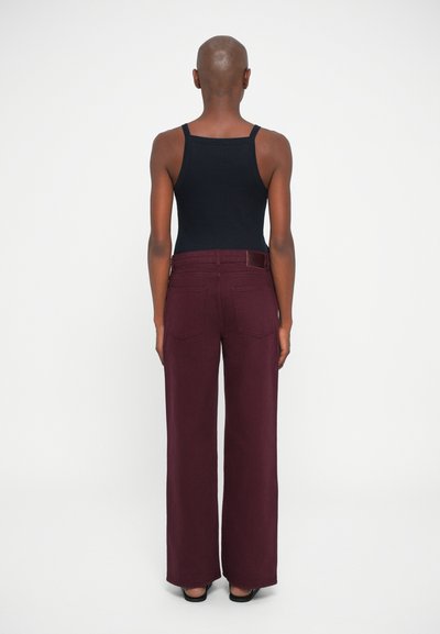 Pantalones anchos burdeos con cintura alta, bolsillos traseros y una textura suave, combinados con una camiseta de tirantes negra.