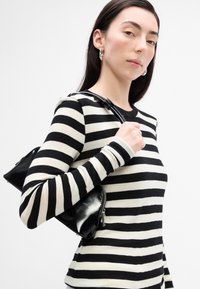 Camiseta de manga larga a rayas blanco y negro hecha de material suave; bolso negro con textura brillante y cremallera plateada llevado sobre el hombro.