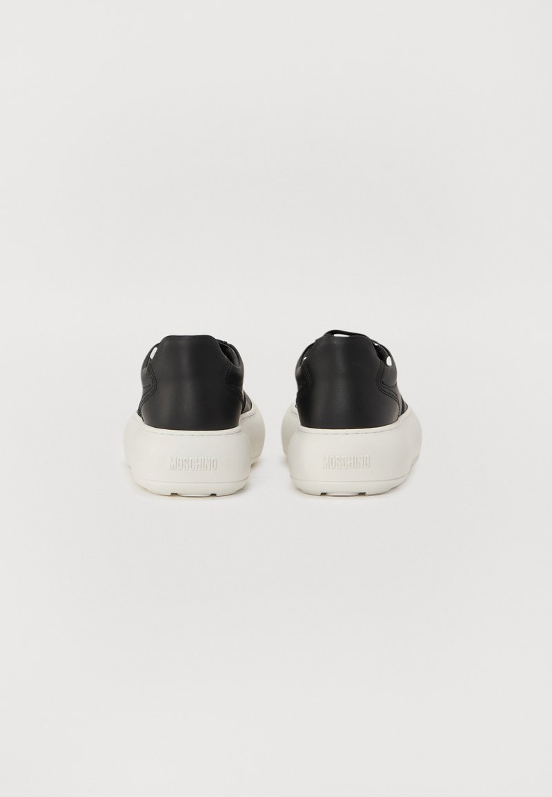 Zwarte leren sneakers met een witte rubberen zool hebben een ronde neus, een achterste tab en een reliëflogo. Glad uiterlijk met een minimalistisch ontwerp.