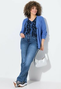 Cardigan azul sobre una blusa negra con estampado, combinado con jeans de un azul claro. Los accesorios incluyen un bolso plateado y zapatillas en blanco y negro.