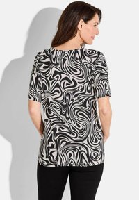 Korte mouwen top in zwart en crème met een draaiend abstract patroon. Zachte stof met een ontspannen pasvorm, ronde halslijn en rechte zoom.