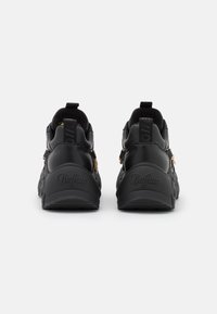 Black sneakers with a textured leather finish, padded cuffs, embossed logo at the heel, and decorative zippers on the sides.
