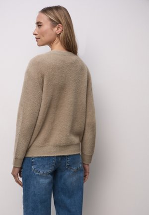 Maglione beige realizzato in tessuto morbido e dalla consistenza testurizzata, con vestibilità comoda, spalle scese e polsini a coste, abbinato a jeans di denim blu.
