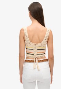 Gehaakte beige crop top met multi-kleurige strepen, verstelbare lace-up rug en brede bandjes. Gecombineerd met witte high-waisted broeken en een gevlochten riem.