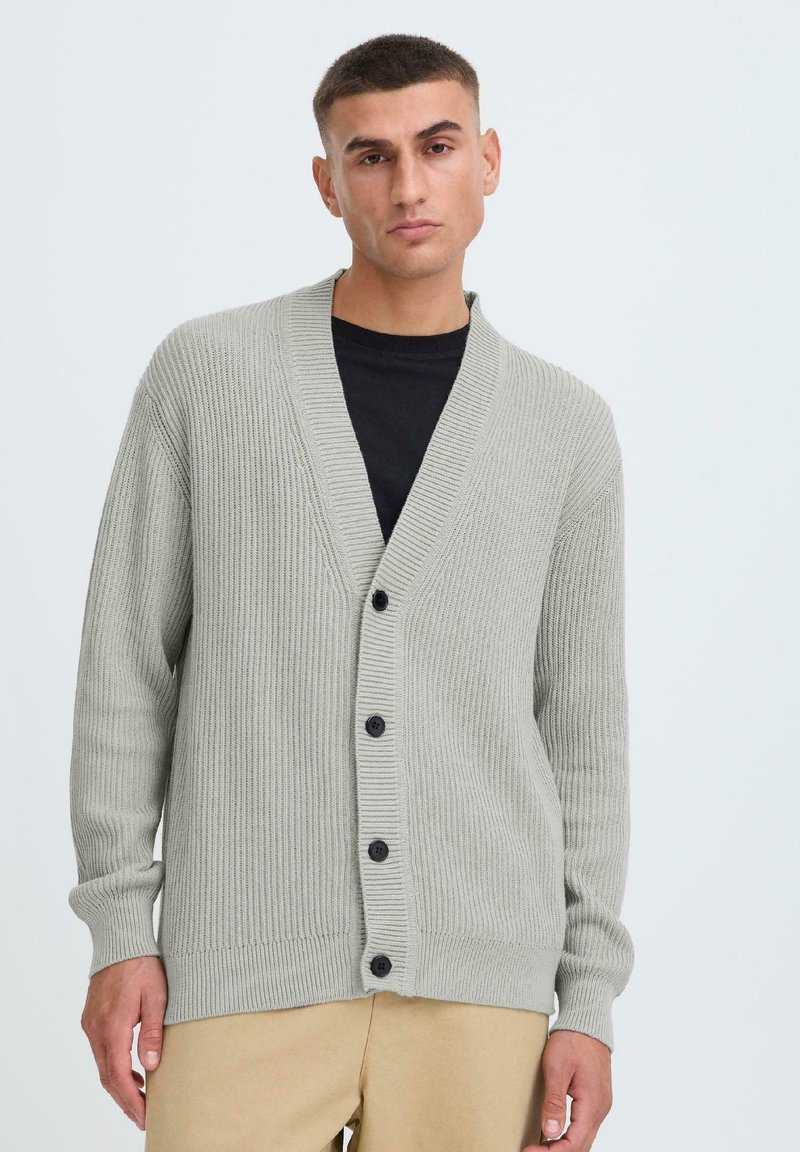 Lichtgrijze cardigan met ribbelstructuur, voorzien van een diepe V-hals, lange mouwen en zes zwarte knopen aan de voorkant.