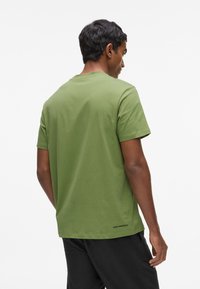 Camiseta de algodón verde oliva con mangas cortas, cuello redondo y sutil branding en la parte inferior de la espalda. Textura suave y ajuste relajado.