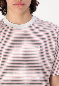 Striped T-shirt in cotton, featuring red, pink, and gray horizontal lines. White ribbed collar and small logo on the chest. Soft texture.