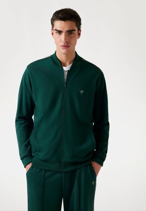 Green zip-up track jacket made of smooth fabric, featuring a stand collar, side pockets, and a small logo in the upper left corner.