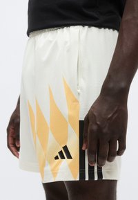 Λευκά σορτς με υφή και κίτρινα σχέδια φλόγας, μαύρες λεπτομέρειες, ελαστική μέση και πλαϊνή τσέπη με φερμουάρ.