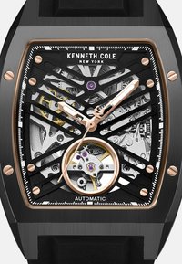Automatische Kenneth Cole Armbanduhr mit schwarzem Skelettzifferblatt, goldenen Akzenten und rundem Gehäuse. Verfügt über filigrane Zahnräder und ein schwarzes Gummiband.