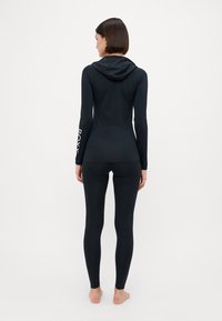 Top sportivo nero a maniche lunghe con cappuccio e leggings, con un design aderente e branding sulla manica. Tessuto liscio e elastico.