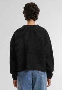 Zwarte gebreide trui met een losse fit, gestructureerd patroon en verlaagde schouders. Gecombineerd met lichtblauwe high-waisted jeans.