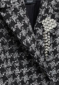 Revers de veste en tweed noir et blanc avec un groupe de broches en strass clairs, facettés, en forme de fleur et une chaîne pendante.