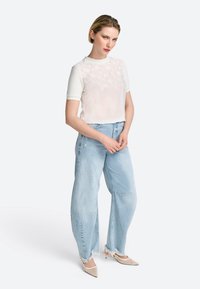 Weißes Oberteil mit floralem Stickdesign auf der Vorderseite, kombiniert mit hellblauen weit geschnittenen Jeans mit fransigen Säumen und lockerem Sitz.