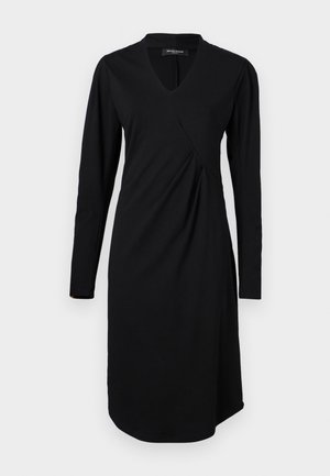 Zwarte jurk met lange mouwen, een V-hals en asymmetrische draping. Gemaakt van zachte stof, heeft het een ronde zoom en subtiele stiksels.