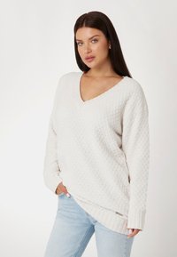 Witte gebreide trui met een V-hals, geribbelde manchetten en zoom. Draag een losse pasvorm over lichtblauwe jeans.